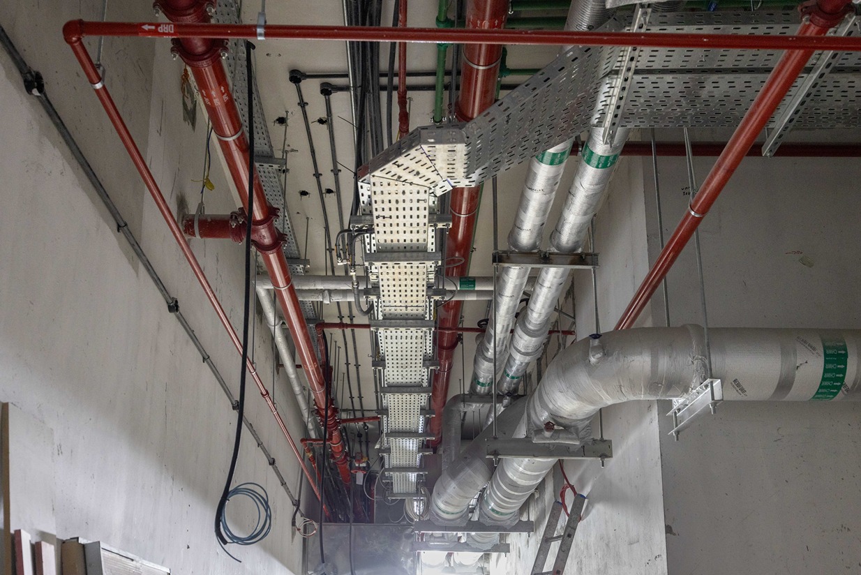 Pearl House By Imtiaz Industrial ceiling with various pipes and conduit, featuring red and silver tubing in a construction setting.
